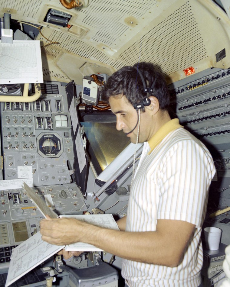 Harrison Schmitt holds documents while standing inside the lunar module simulator