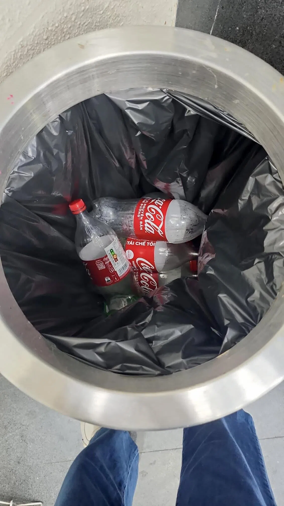 The man threw the empty 1.5 liter coke bottles into the rubbish bin.