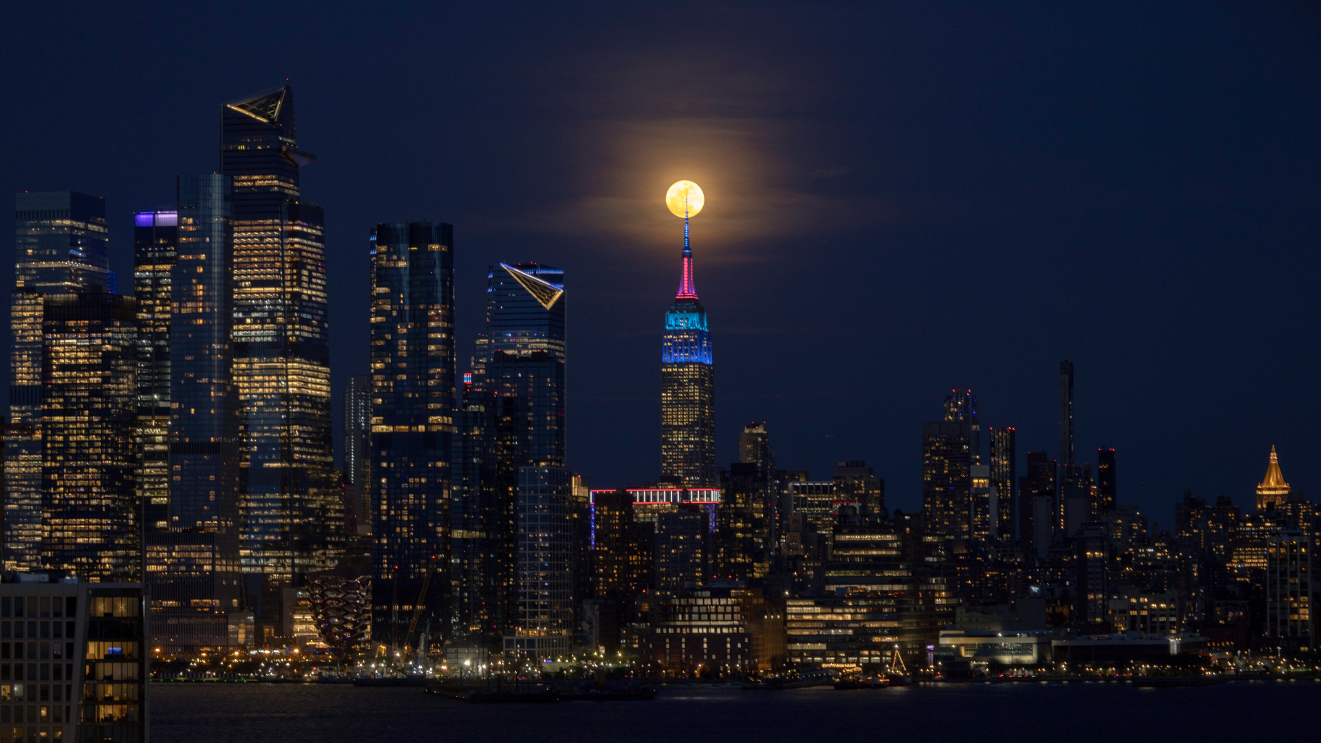 A full yellow moon is depicted shining between two giant towers in the night sky.