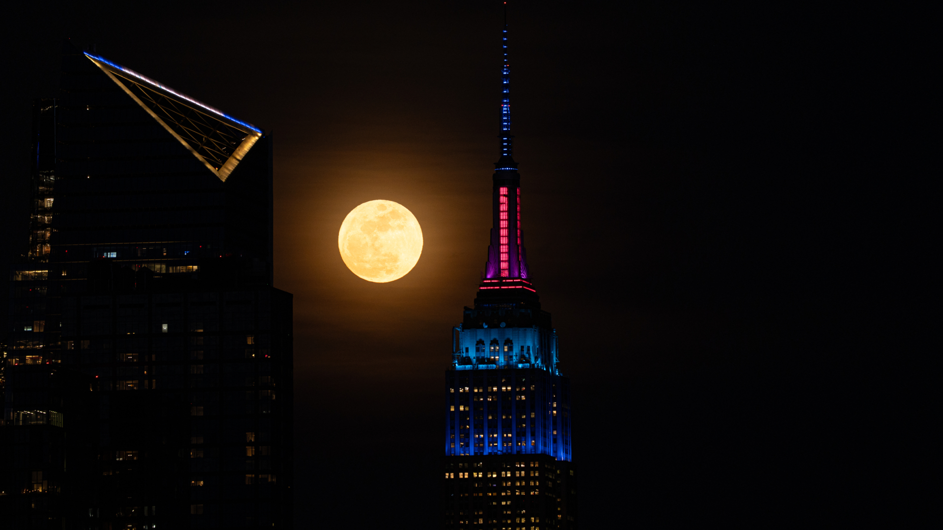 A full yellow moon is depicted shining between two giant towers in the night sky.