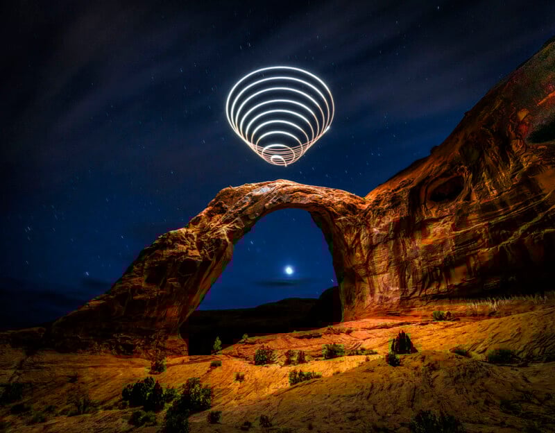 A natural tablet under a starry night sky, with spiral light trails above it, ​​​​​​​​​to create a futuristic effect. The landscape is illuminated, highlighting red rock formations and scattered vegetation.
