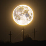 A full orange moon is depicted shining above three crosses on the hill.