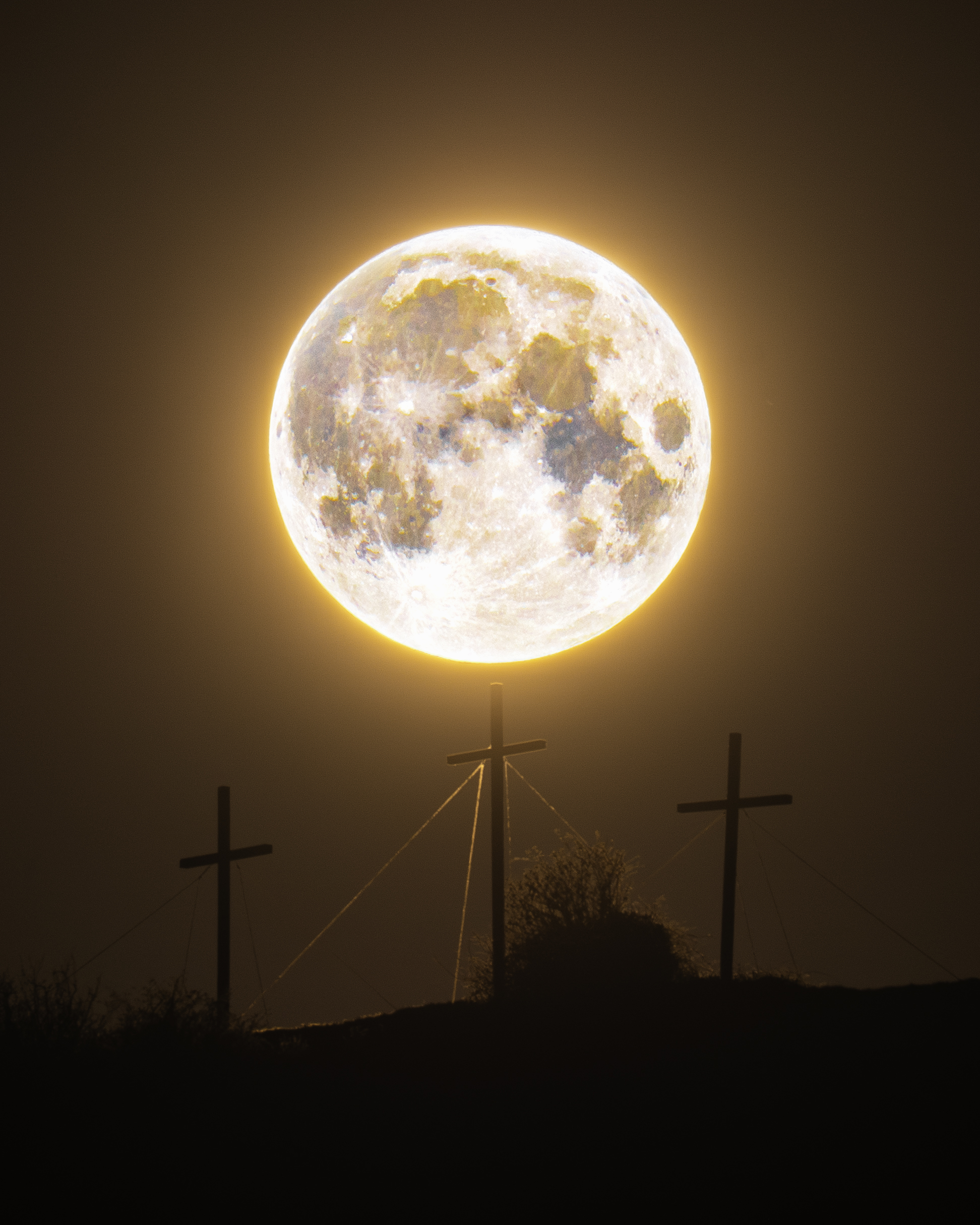 A full orange moon is depicted shining above three crosses on the hill.