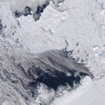 Dark open water south of thin, broken sea ice near Franz Josef Land, with thin clouds covering part of the area.