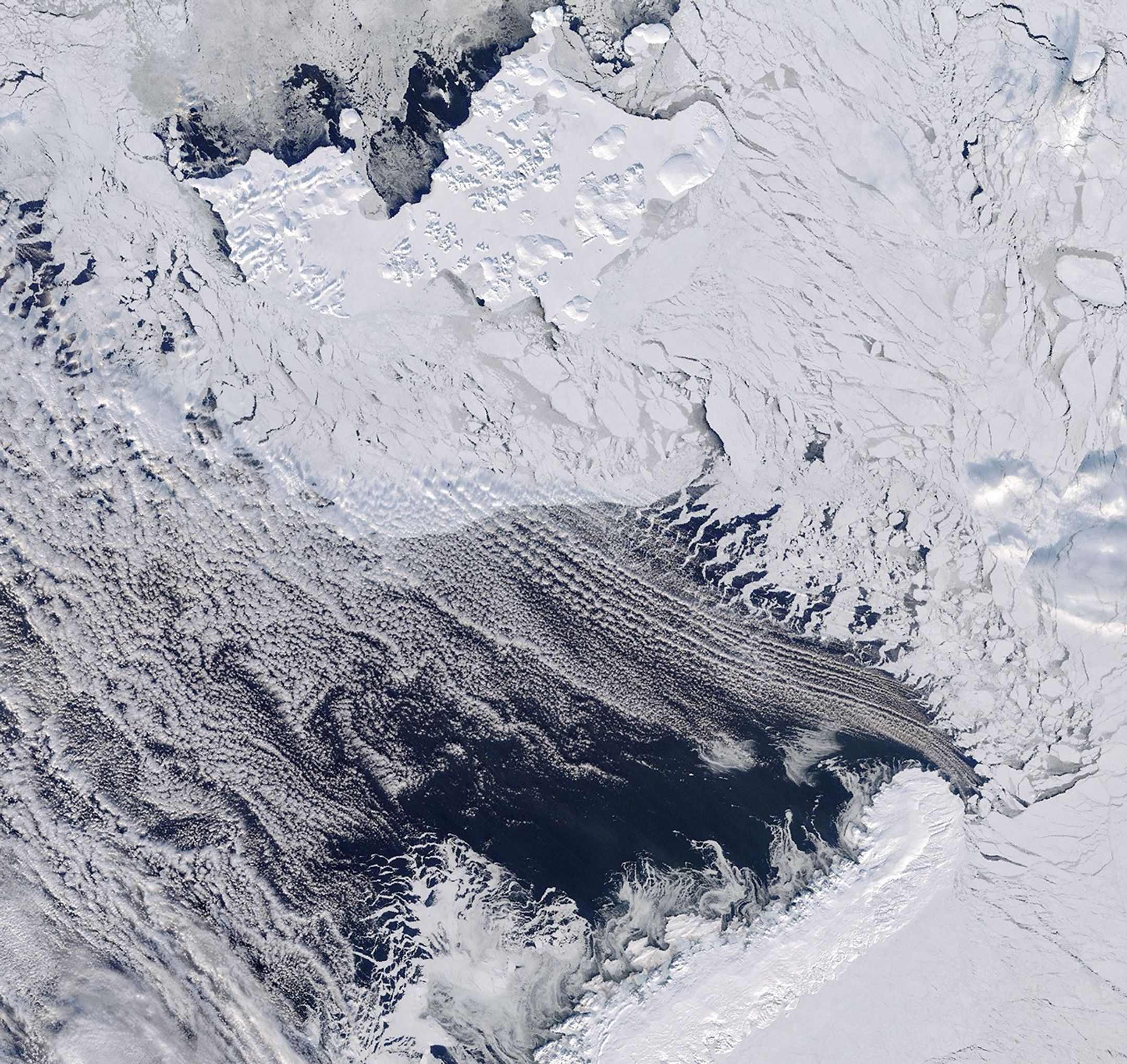 Dark open water south of thin, broken sea ice near Franz Josef Land, with thin clouds covering part of the area.