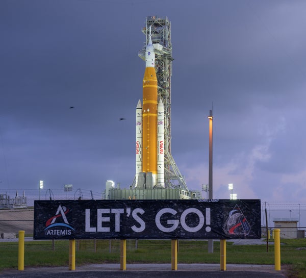 The Space Launch System rocket and Orion crew capsule sit on the pad, waiting for launch. A sign with the words