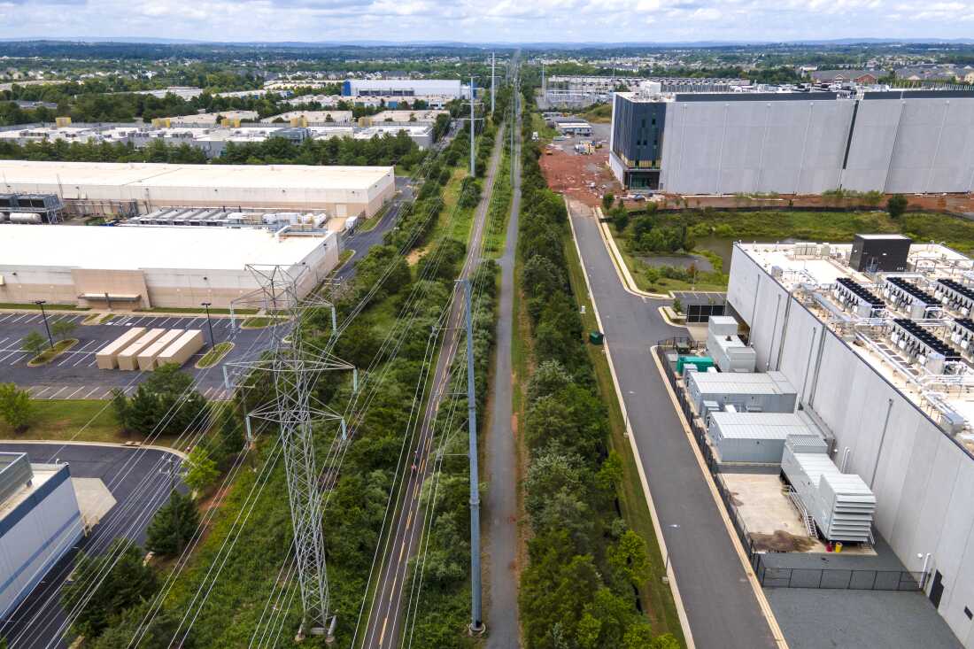 High-power transmission lines stretch across the green space, supplying electricity to the large, box-shaped data centers that sit on either side of the campus in Ashburn, Virginia.